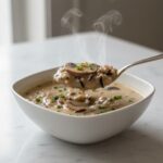 Spoon lifting Cream of Mushroom & Wild Rice Soup, showing creamy texture.